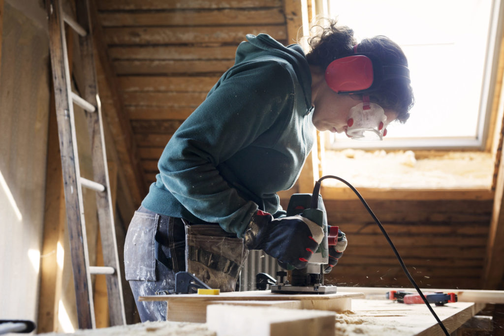 Woman using power tool while renovating old attic